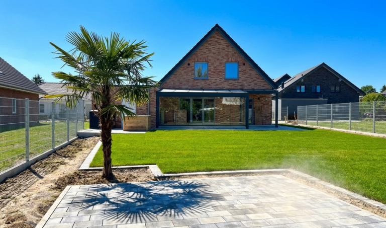 Moderns -Einfamilienhaus met terrasoverkapping en glazen schuifwand van aluminium, Sommerfoto met Palme en Rasen